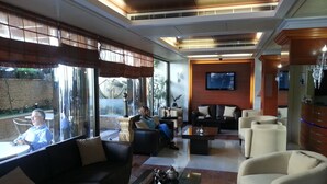 A spacious lobby with a seating area, a television mounted on the wall, and a bar area with a counter and bar stools. - Duroy Hotel (Beirut)