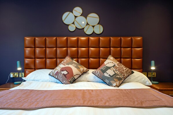 Un lit bien fait, avec une tête de lit marron, deux coussins à motifs et un plaid marron.