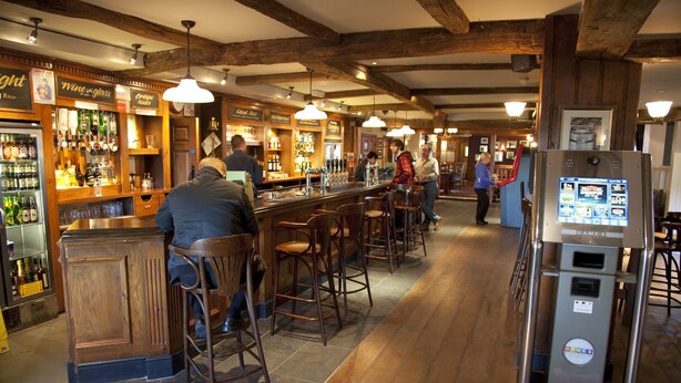 A bar area with wooden furniture, a bar counter, and a refrigerator with a digital display. - The Conningbrook Hotel (Ashford)