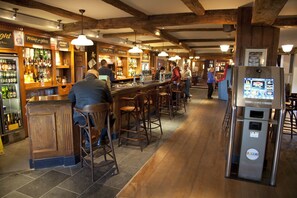 A bar area with wooden furniture, a bar counter, and a refrigerator with a digital display. - The Conningbrook Hotel (Ashford)