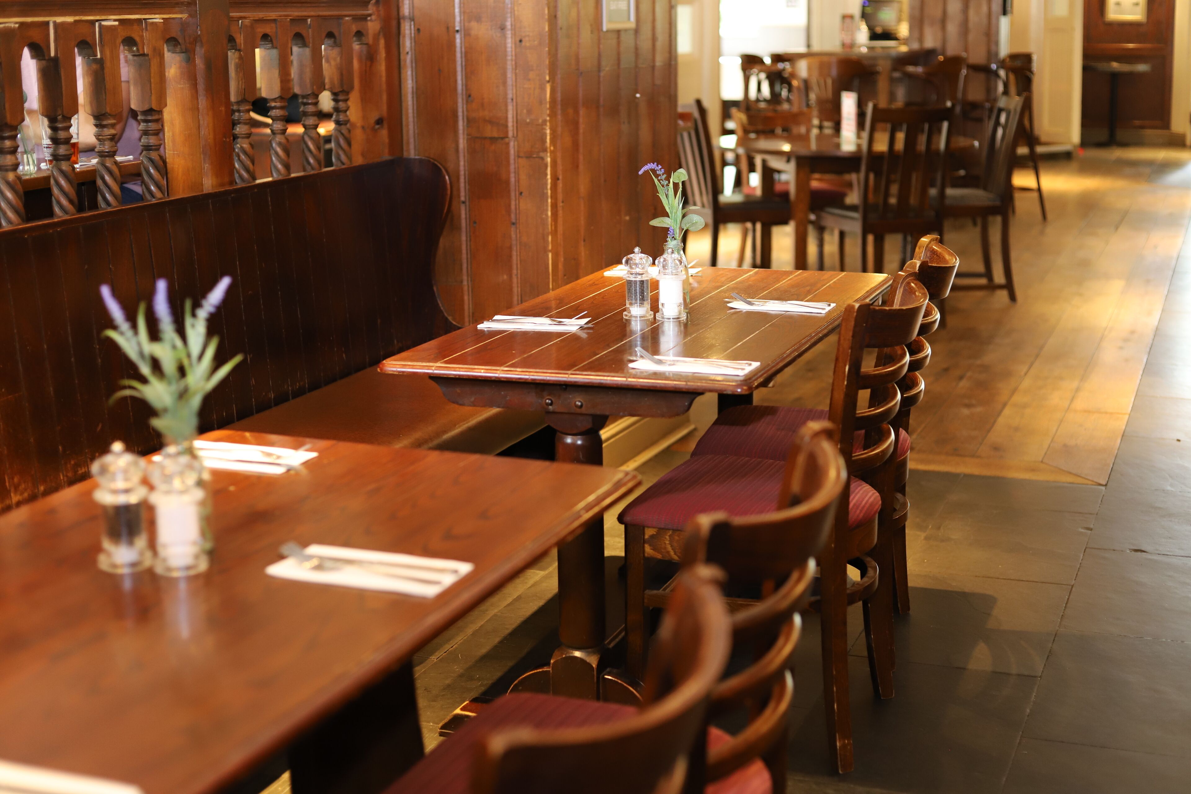 A restaurant with wooden tables and chairs, some with red cushions.