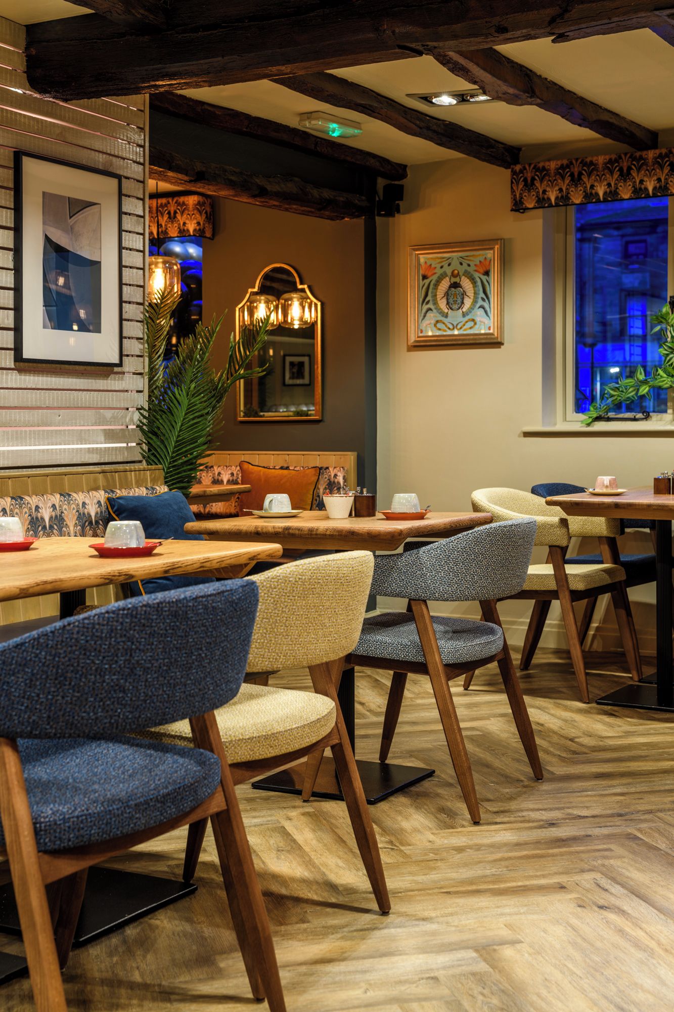 Interior de restaurante con mesas de madera, sillas tapizadas y un piso con patrón de espiga.