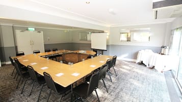 Un salón de conferencias con una gran mesa, sillas, una pizarra y una ventana con cortinas.
