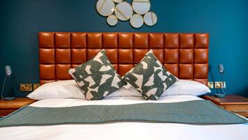 A bed with a brown leather headboard, two camouflage pillows, a white pillow, and a blue throw blanket.
