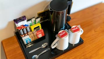 A tray with a coffee maker, two mugs with Biscoff biscuits, a spoon, and various packaged food items.
