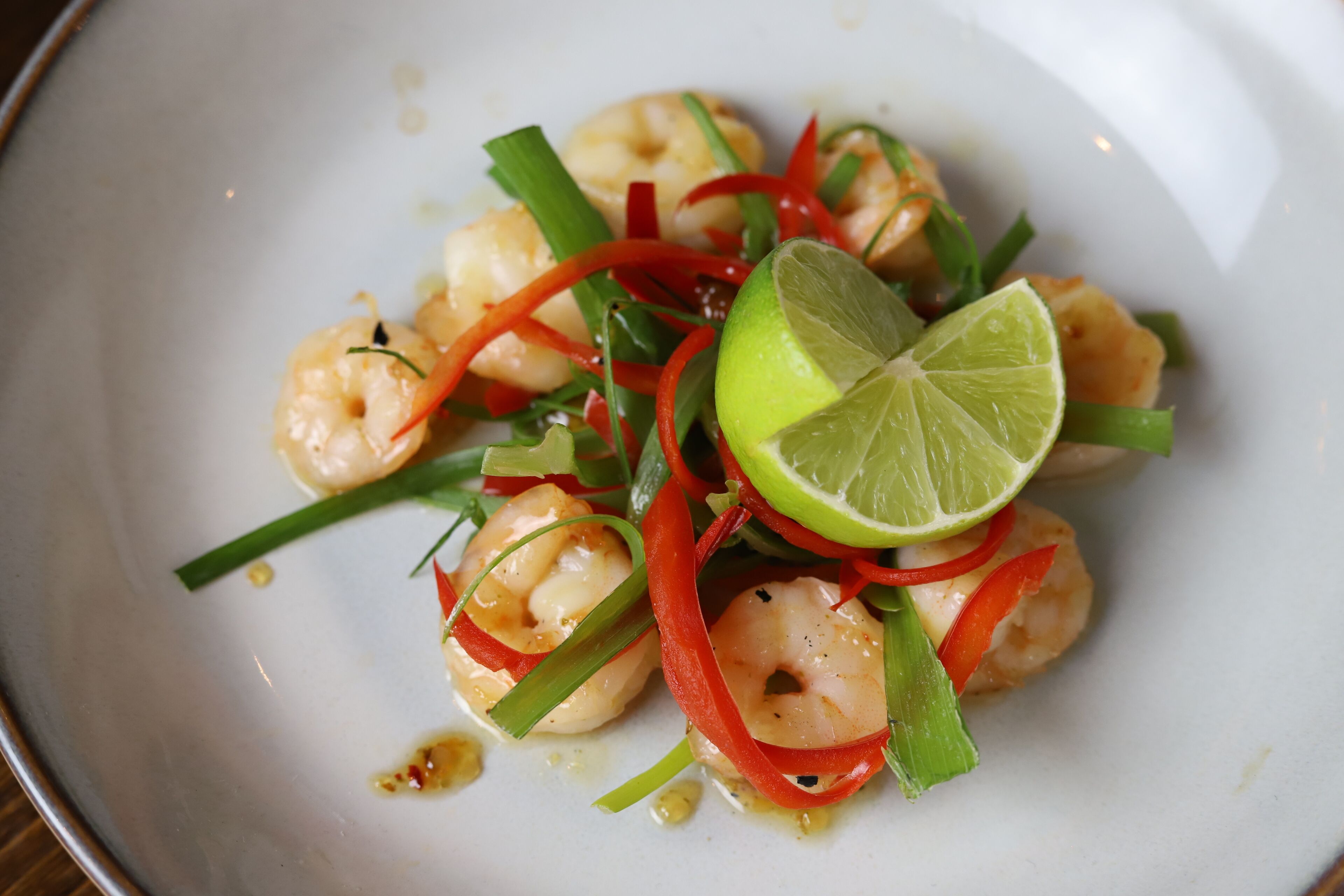 Un plato de camarones con adorno de lima y pimiento rojo.