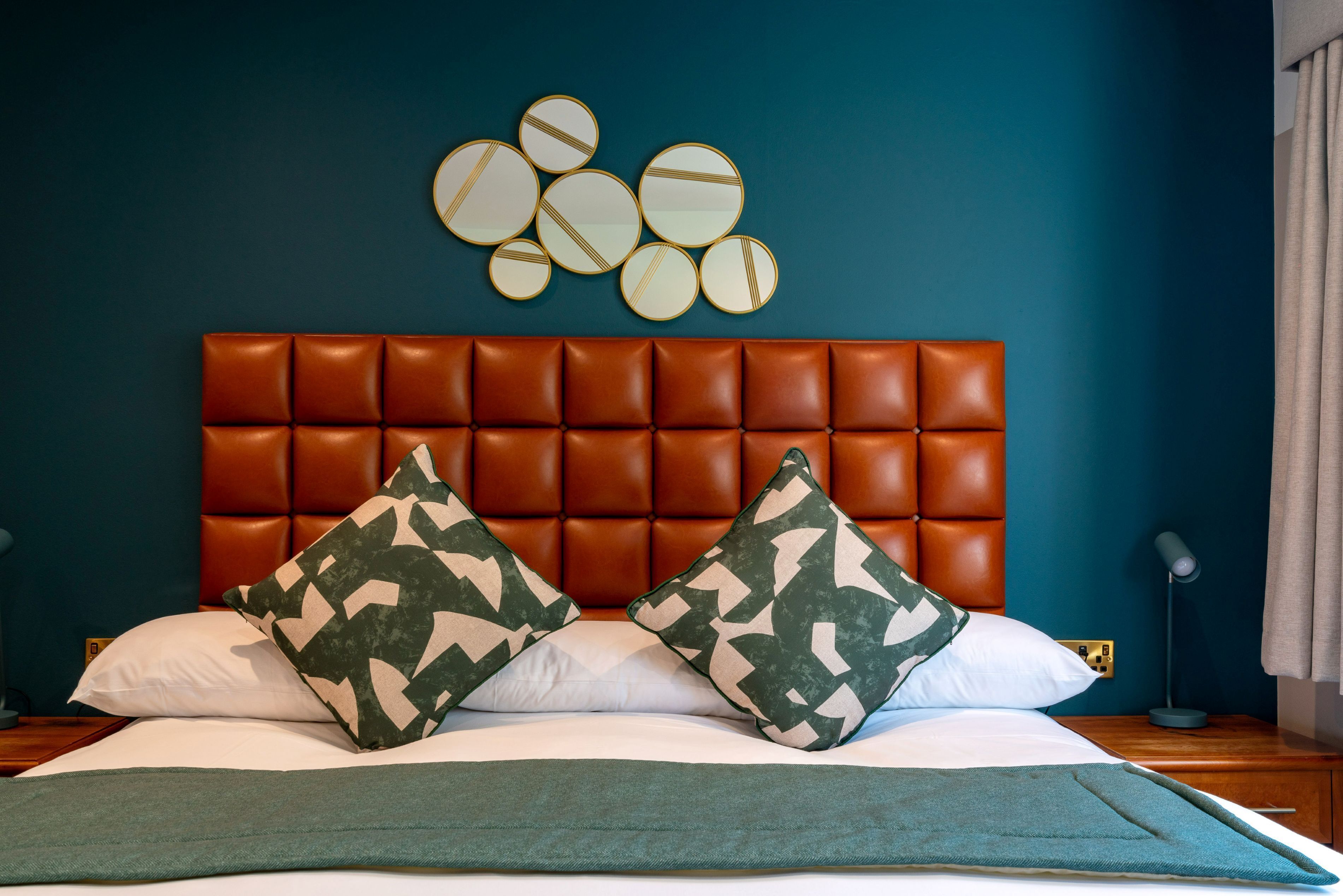 A bedroom with a tufted headboard, two patterned pillows, a green throw, and wall decor.