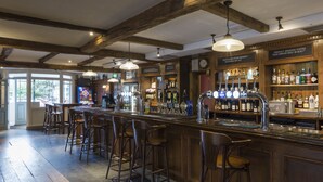A bar area with wooden beams, bar stools, and a variety of bottles and glasses. - The Conningbrook Hotel (Ashford)