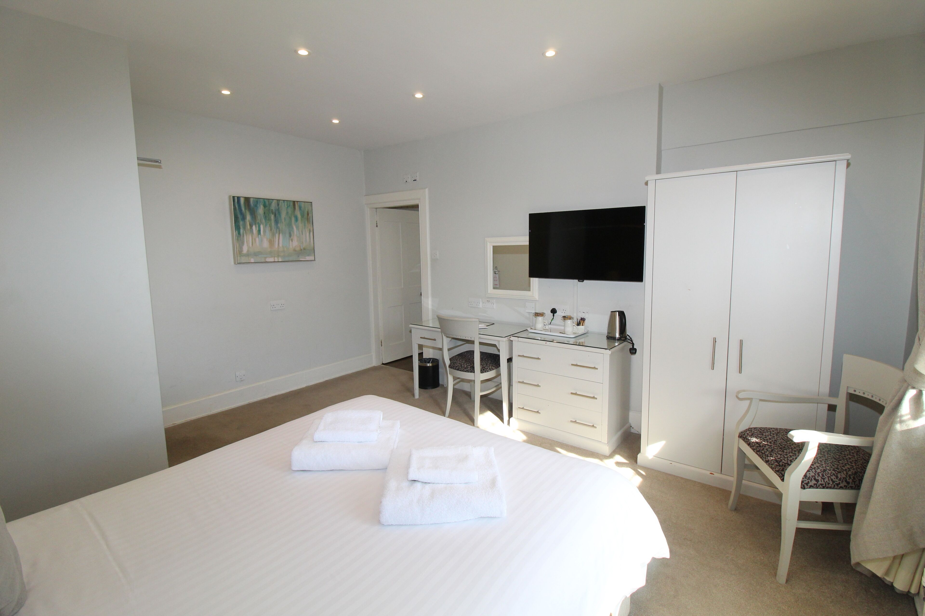 A hotel room with a large bed, a desk, a chair, a wardrobe, and a television.