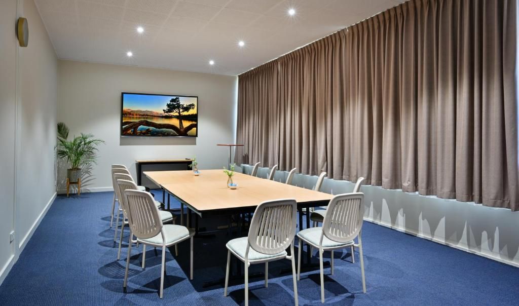 A conference room with a long table, chairs, a painting on the wall, and a curtain.