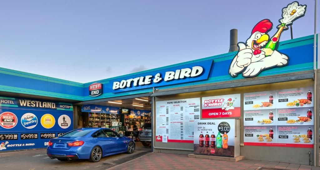 A storefront with a prominent 'BOTTLE & BIRD' sign, a menu board, and a blue car parked in front.