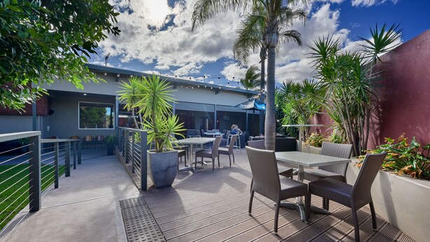 An outdoor patio area with tables and chairs, surrounded by plants and a modern building. - Westland Hotel Motel (Whyalla Norrie)
