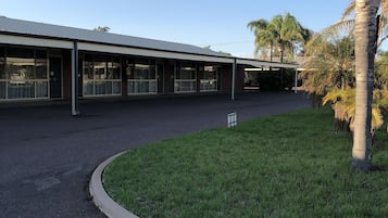 A building with a covered outdoor area, a grassy area with a palm tree, and a clear sky.