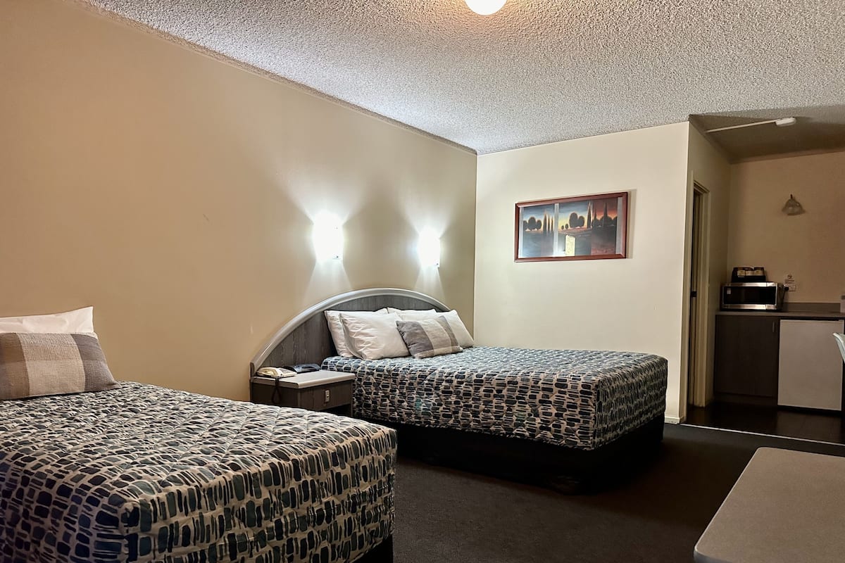 A hotel room with two beds, a desk, a microwave, and a painting on the wall.