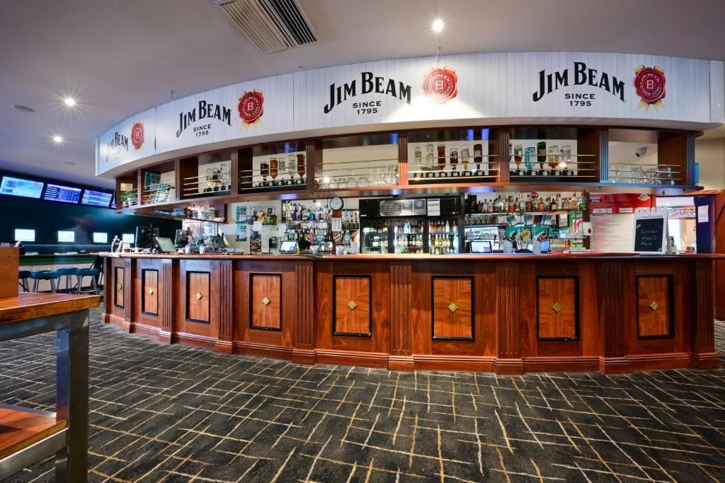 A bar area with a curved counter, multiple shelves of bottles, and a digital menu display.