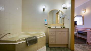 A bathroom with a large bathtub, a vanity with a mirror, and a chair.