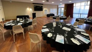 A conference room with multiple tables set for dining, equipped with chairs, tables, and a projector screen. - Westland Hotel Motel (Whyalla Norrie)
