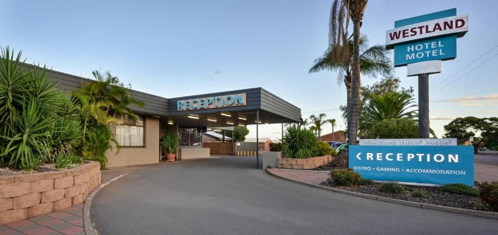Una recepción de hotel con un cartel que indica 'Westland Hotel Motel' y 'Recepción', con servicios como 'Bistro, Juegos, Alojamiento'.