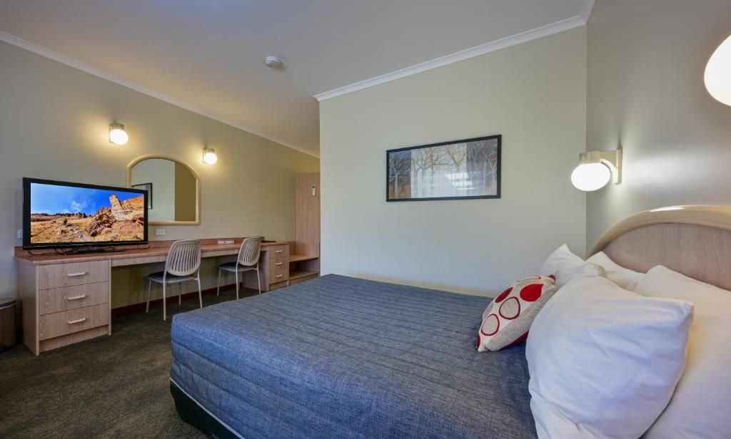 A hotel room with a bed, a desk, a chair, a television, and a framed picture on the wall.