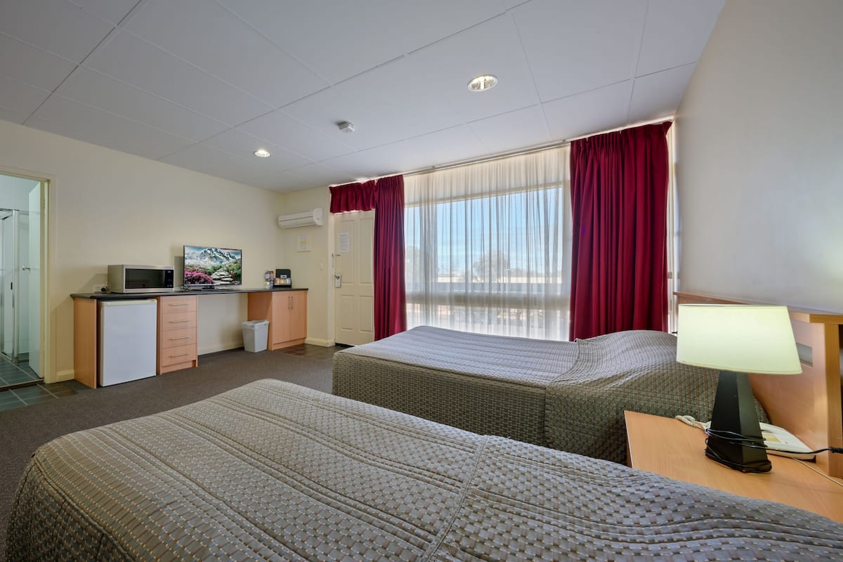 A hotel room with two beds, a desk with a computer, a microwave, and a TV.