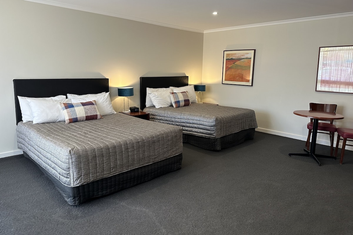 A hotel room with two beds, a small table, and a chair.