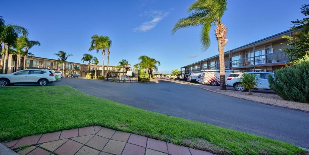 A street view of a hotel with a parking lot, palm trees, and a clear sky.