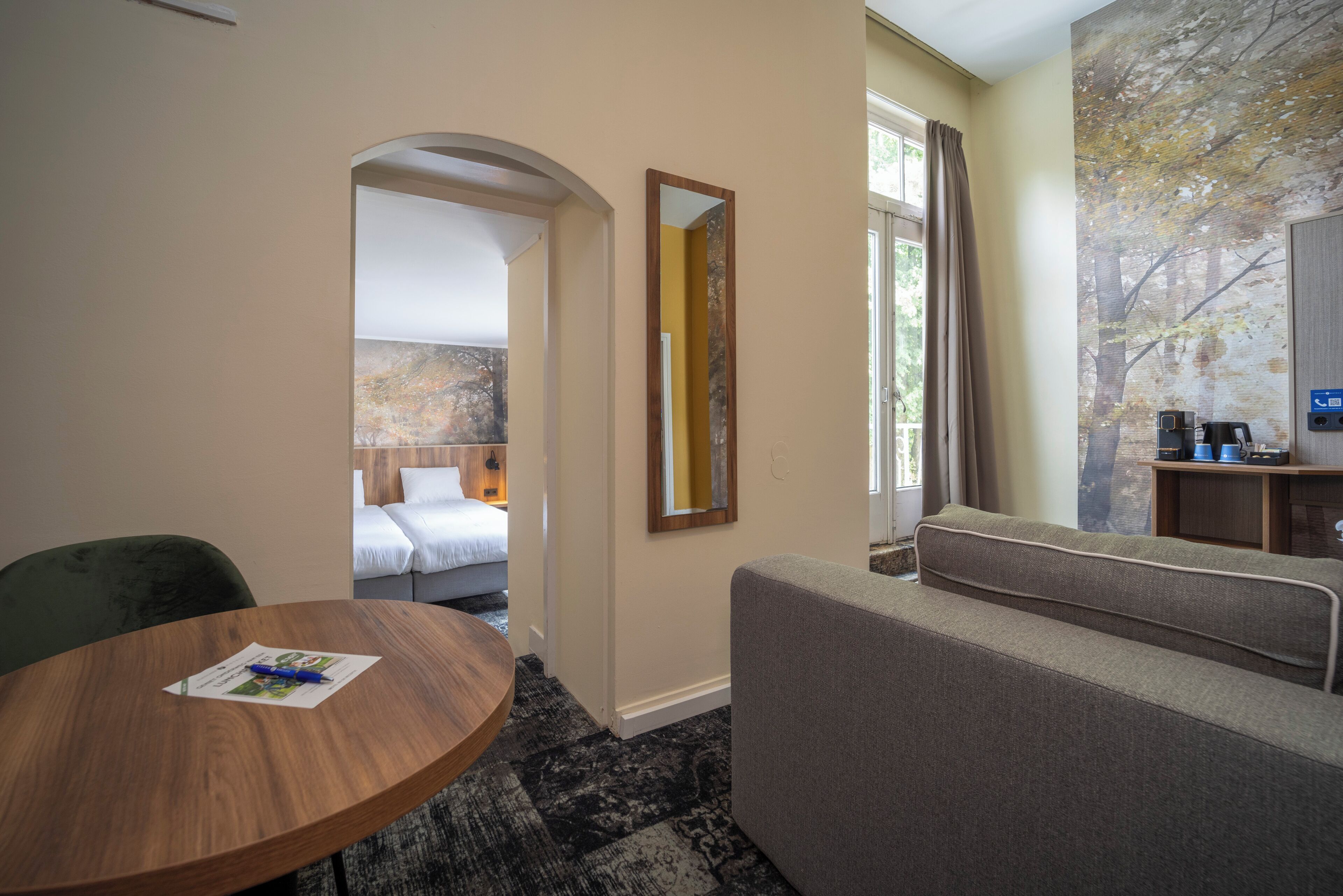 A hotel room with a bed, a sofa, a round wooden table, and a mirror.