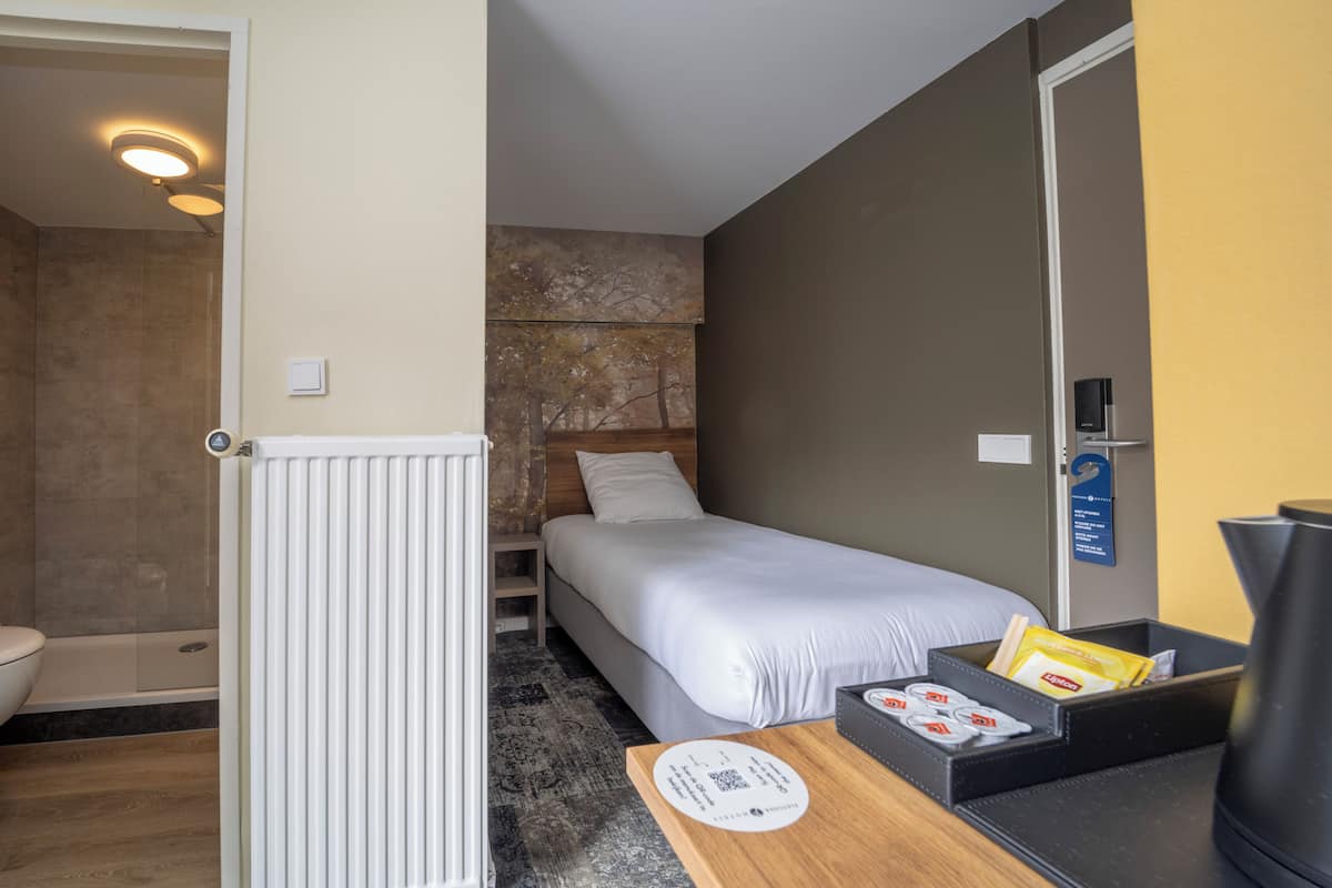 Hotellihuone, jossa on sänky, pieni pöytä, jossa on tarjoilualusta hygieniatuotteille, suihkutila ja näkymä ulos.