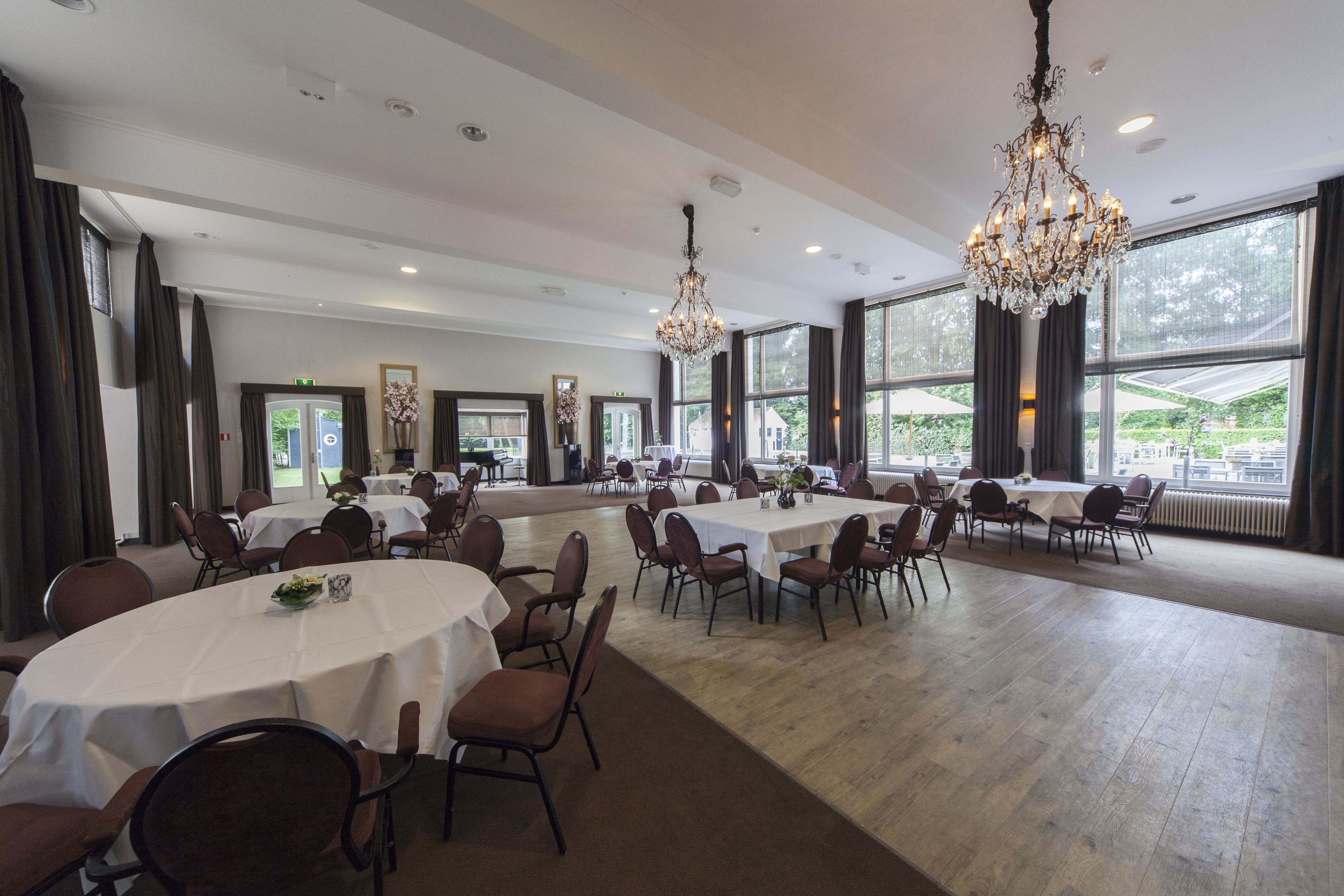 Un amplio salón de banquetes con mesas redondas, sillas, candelabros y grandes ventanales que ofrecen vistas al exterior.