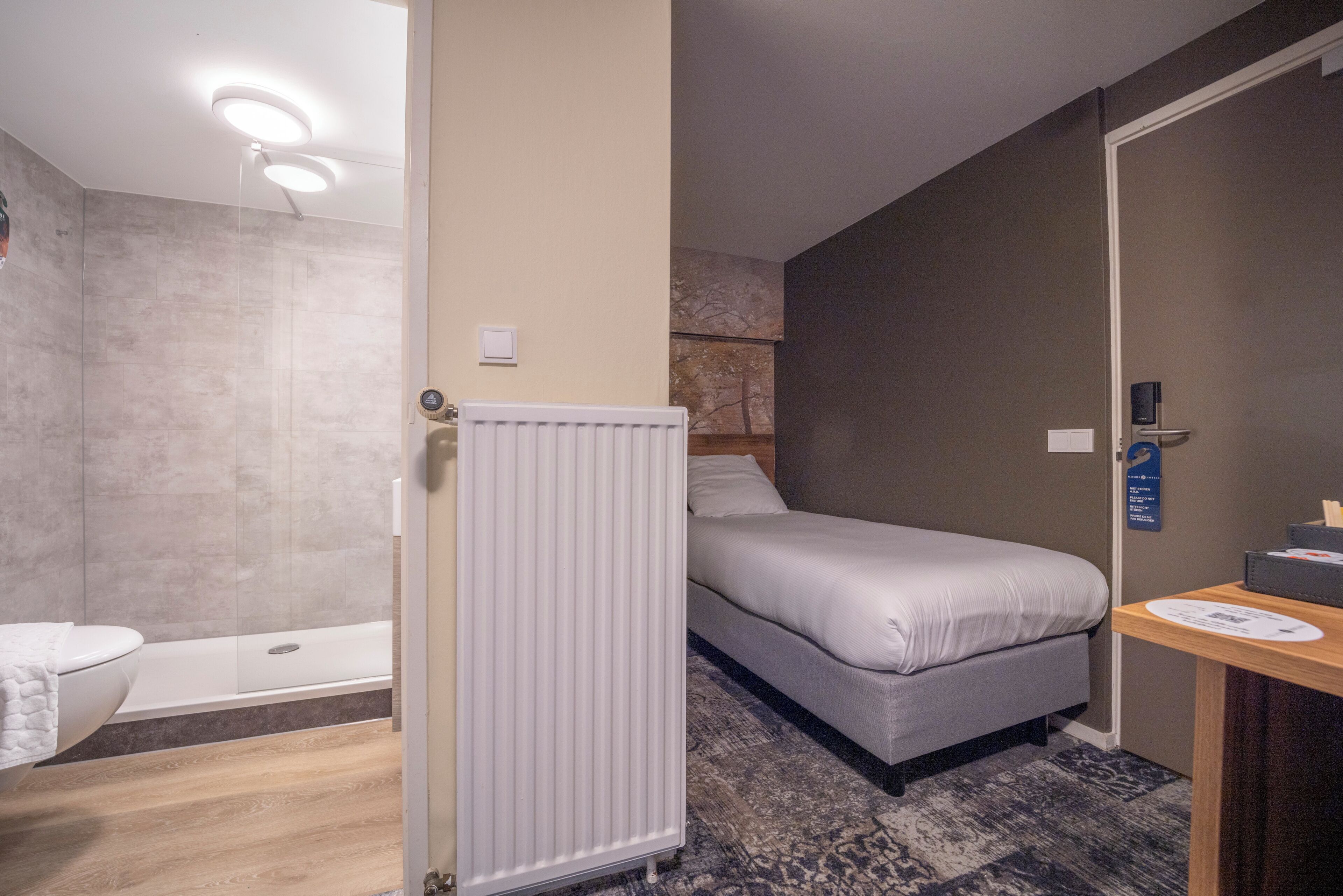 A hotel room with a bed, a bathroom with a bathtub, and a radiator.