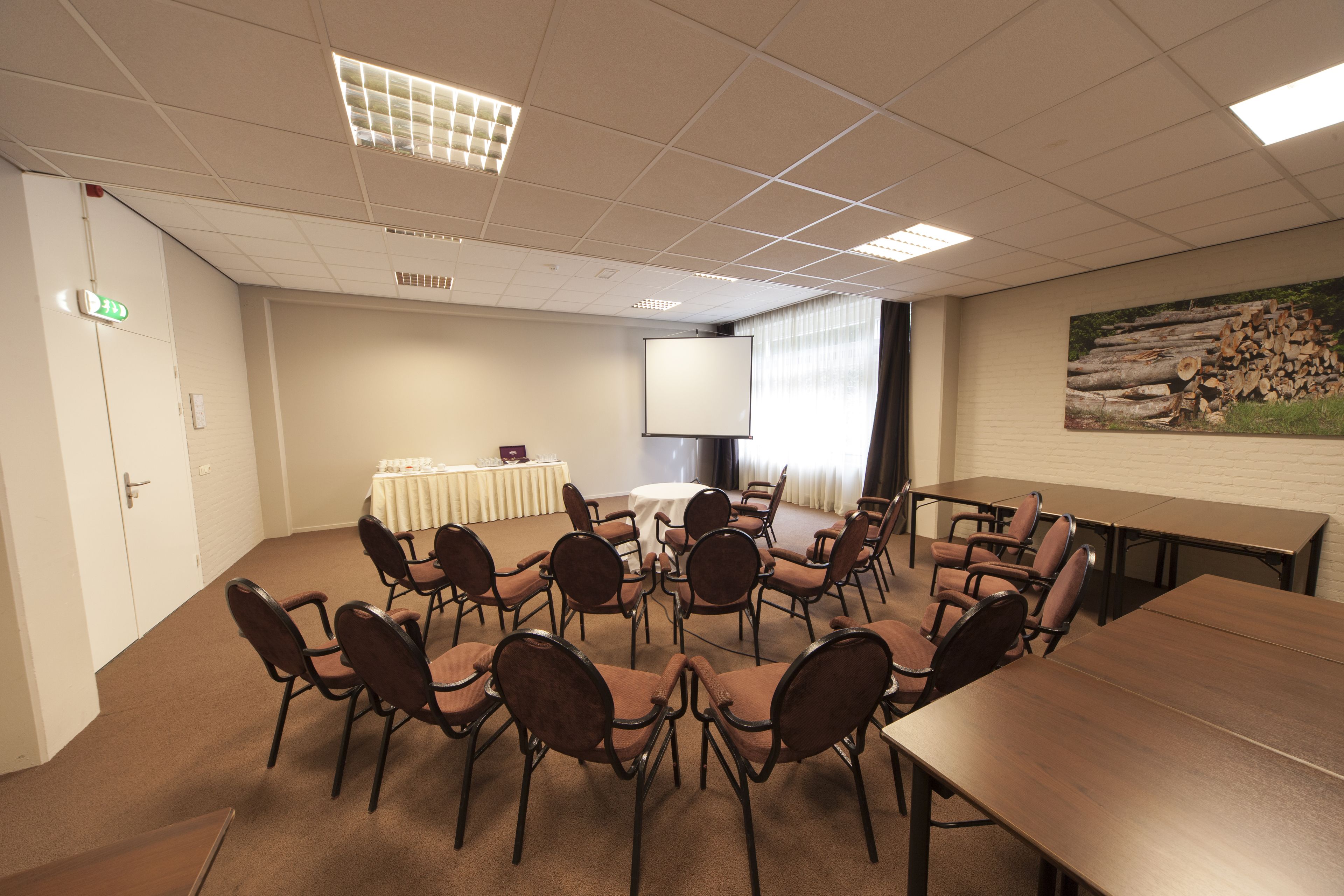 Ein Konferenzraum mit langem Tisch, mehreren Stühlen, einer Projektionsleinwand und einem Tisch mit weißer Tischdecke.