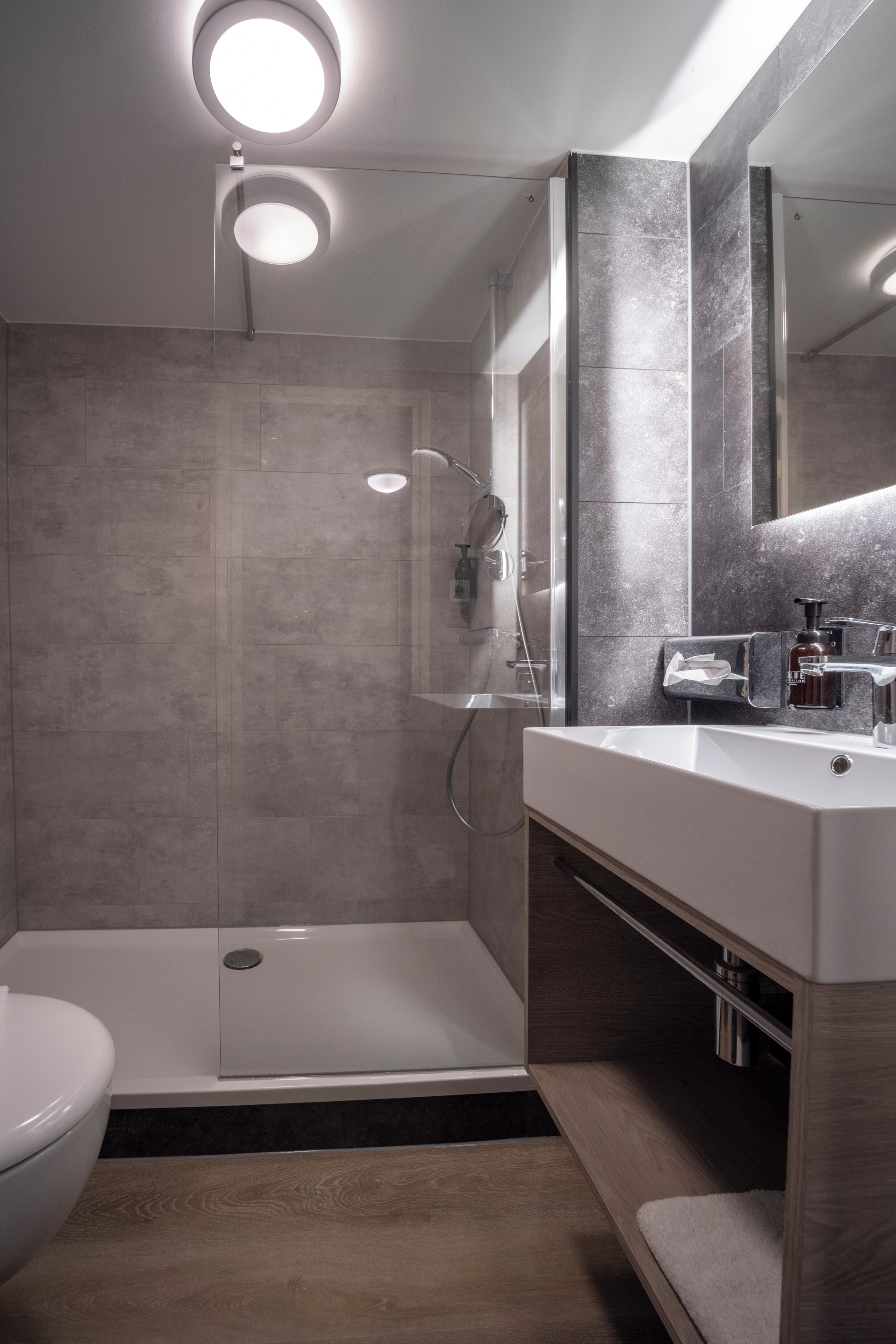 Une salle de bain moderne dotée d’une douche à l’italienne, d’un grand miroir et d’un meuble-lavabo avec un évier et un porte-serviettes.