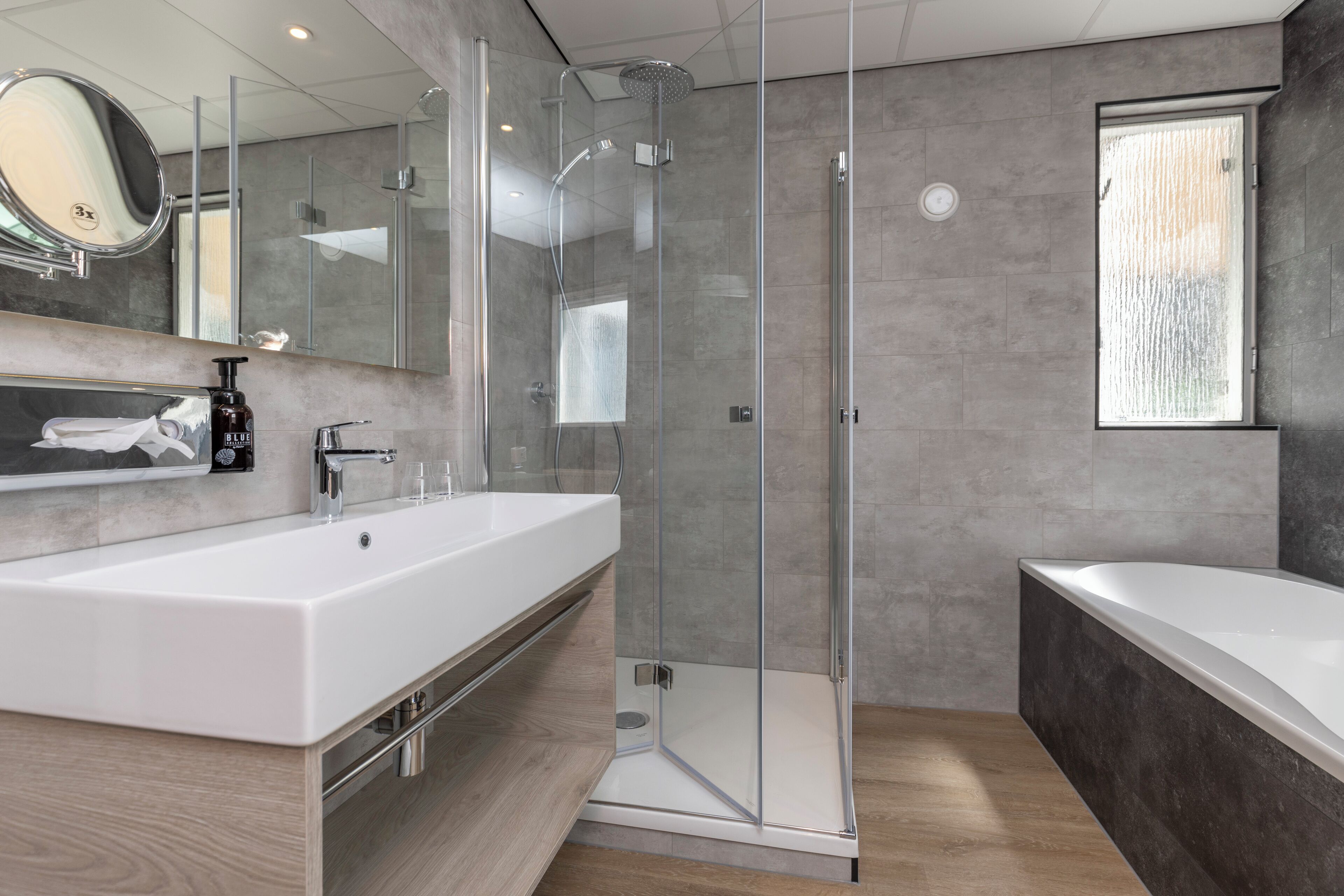 Een moderne badkamer met een grote witte wastafel, een douche met glazen wanden en een vrijstaand bad.
