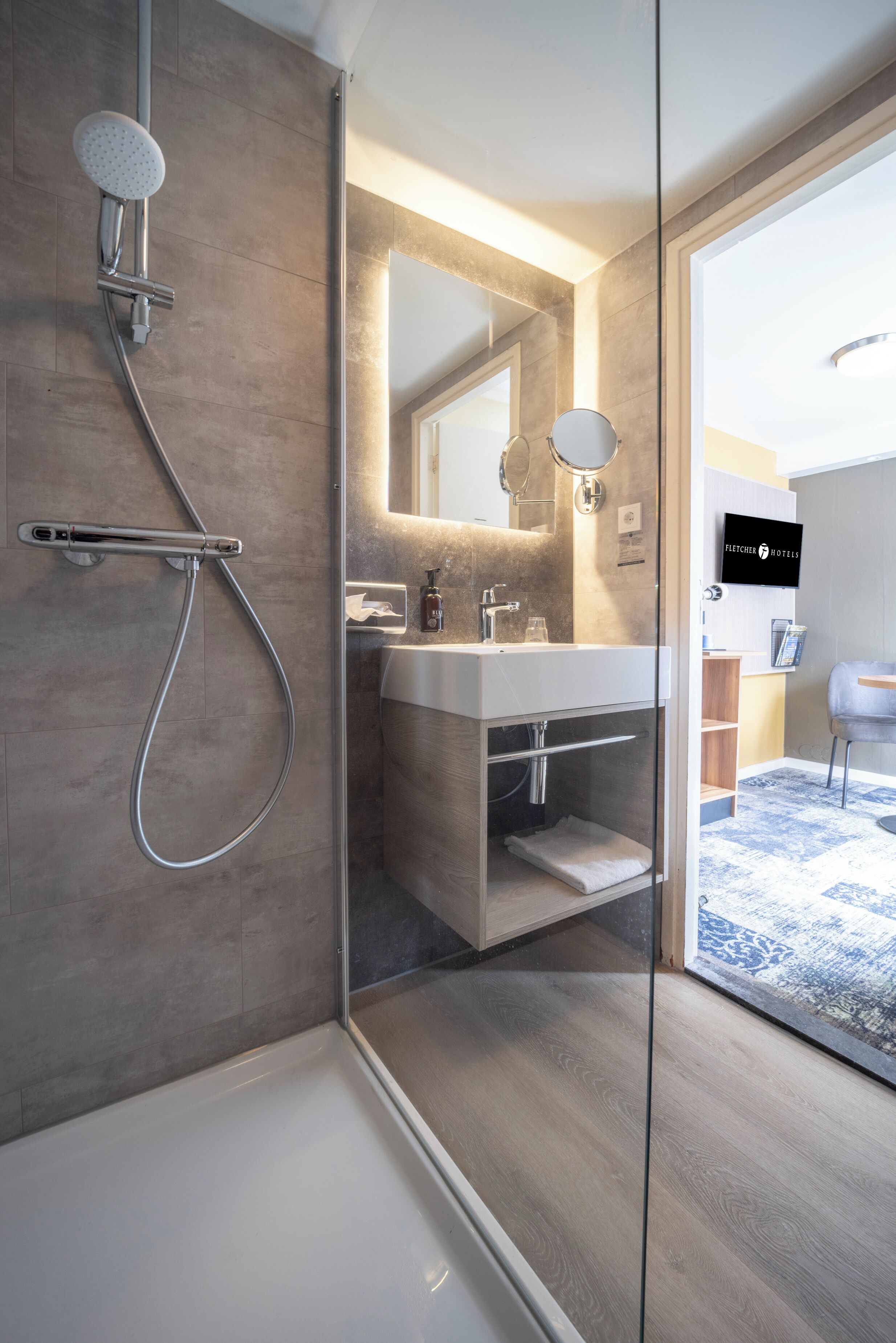 Un baño moderno con ducha de vidrio, un espejo grande y tocador con lavabo y barra para toallas.