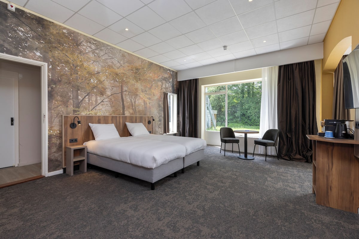 Hotellihuone, jossa on suuri sänky, työpöytä, tuoli ja näkymä ulos.