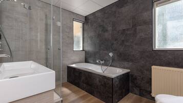 Un baño moderno con ducha de vidrio, bañera independiente y un amplio ventanal que proporciona luz natural.
