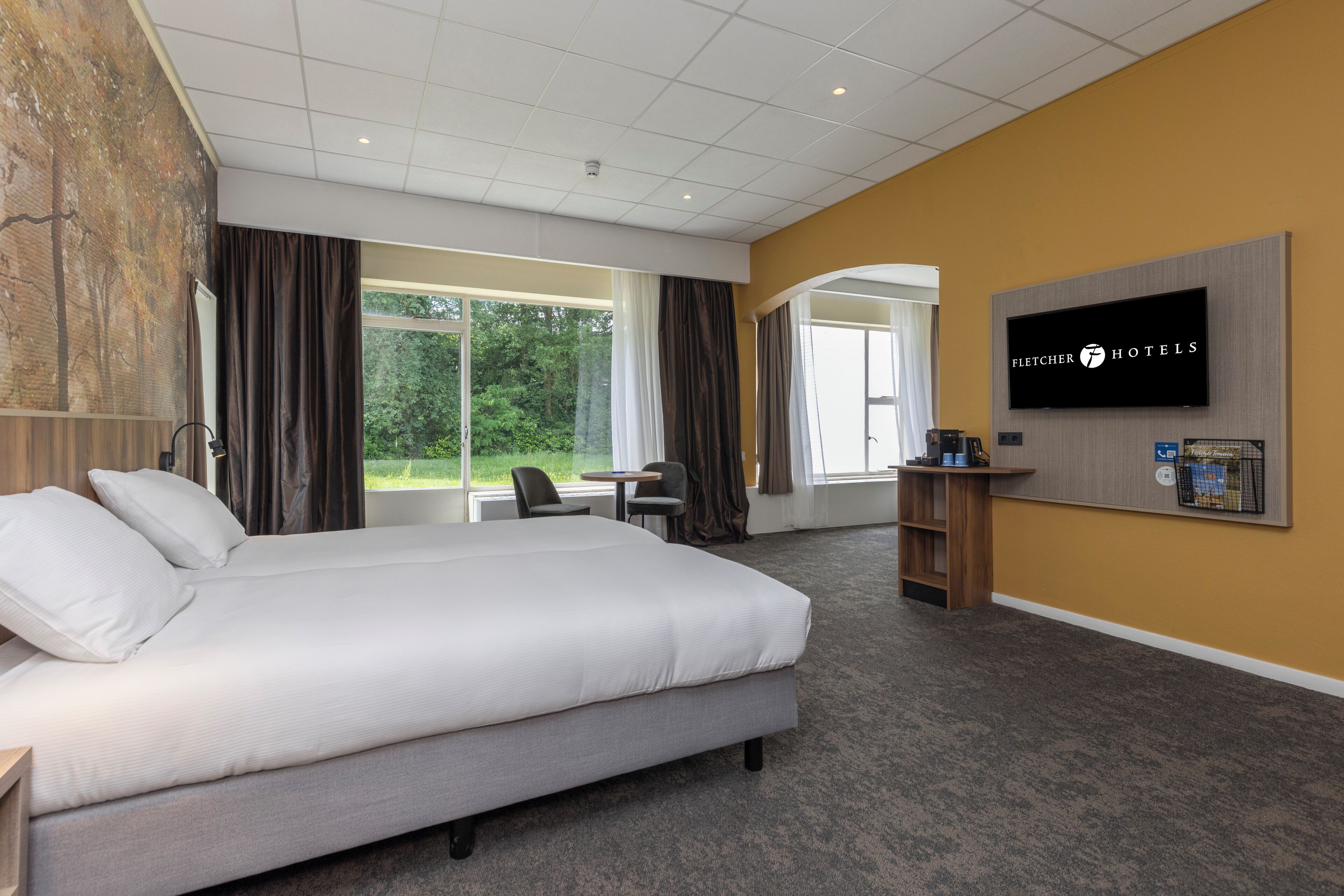 Een hotelkamer met een groot bed, een bureau, een stoel, een televisie en uitzicht op de omgeving.