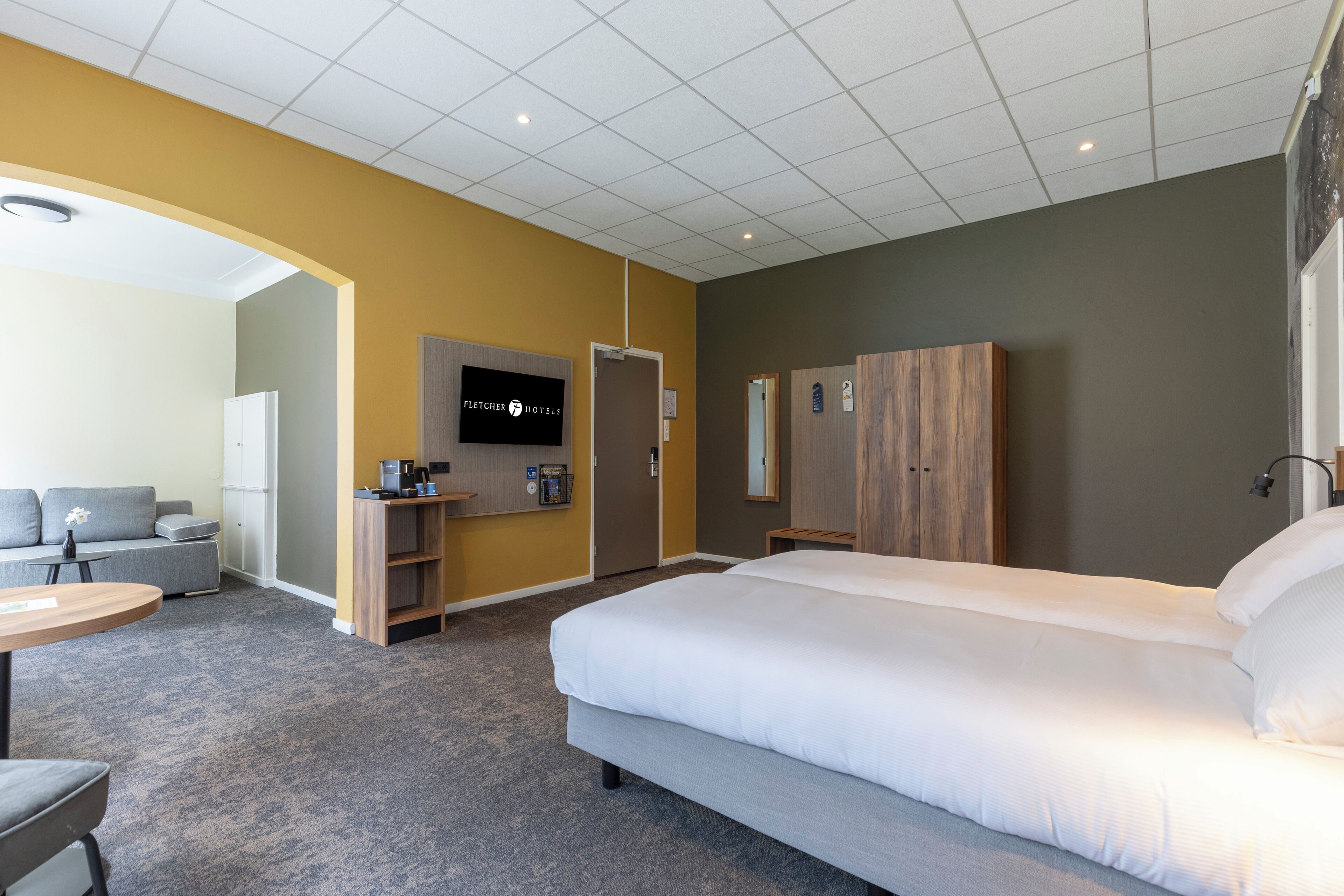 Ein Hotelzimmer mit einem großen Bett, einer Couch, einem Schreibtisch, einem Fernseher und einem Kleiderschrank.