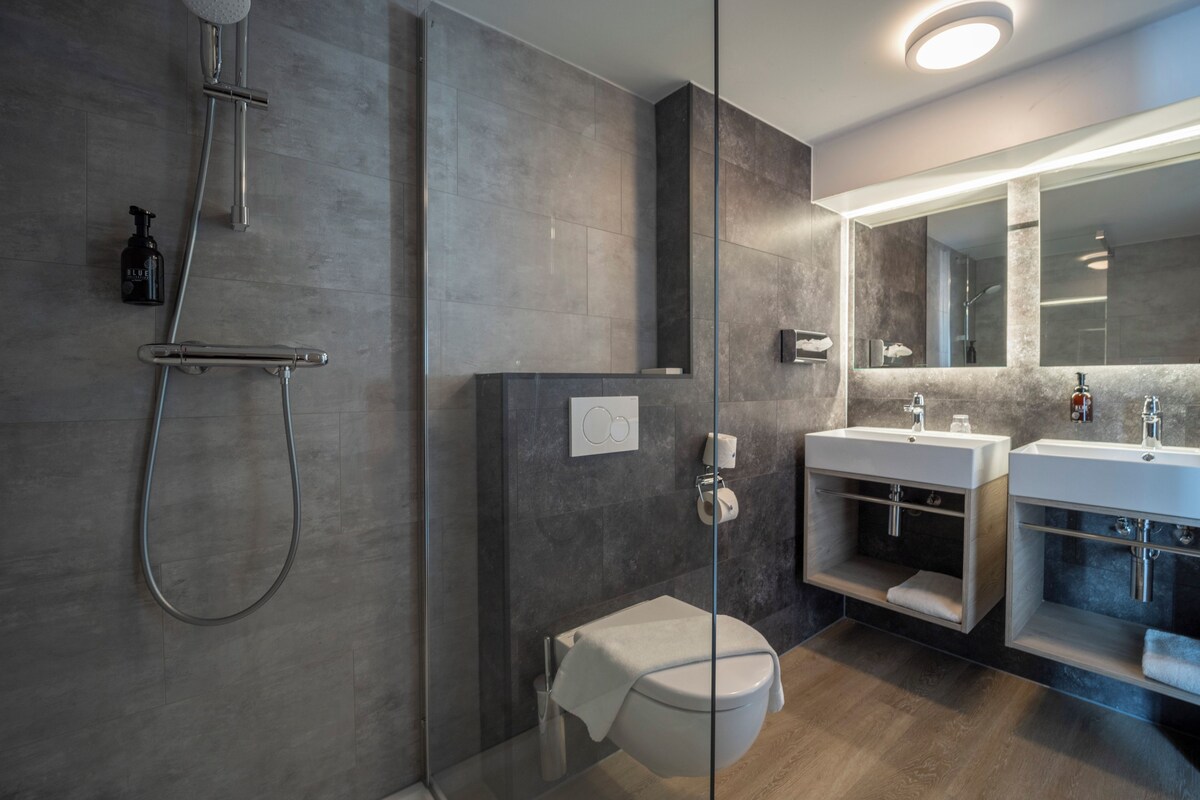A modern bathroom with a glass-enclosed shower, a toilet, and two sinks with vanity cabinets.