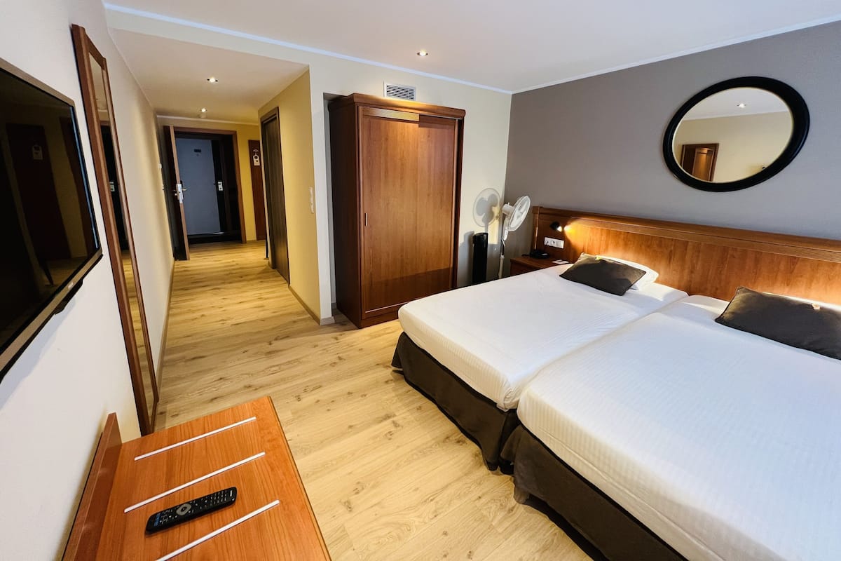 A hotel room with a bed, bedside table, mirror, and a hallway leading to other rooms.