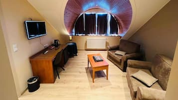 Quarto de loft aconchegante com teto curvo, uma escrivaninha, um sofá e uma televisão.