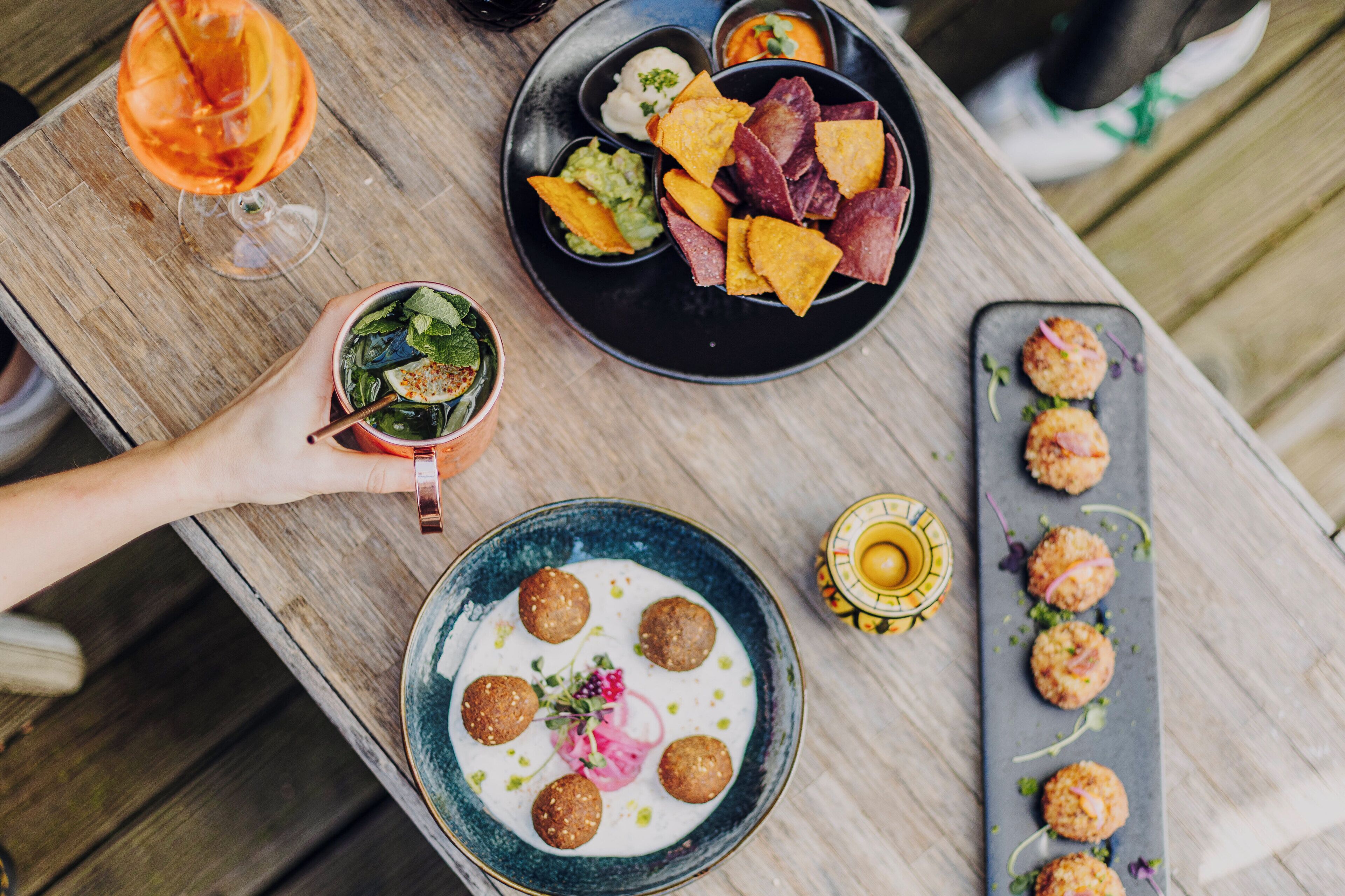 A wooden table with various dishes including a salad, nachos, and meatballs, suggesting a casual dining setting.