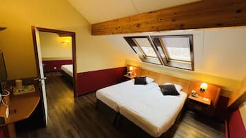 A hotel room with two beds, wooden ceiling beams, a skylight, and a small desk with a lamp.