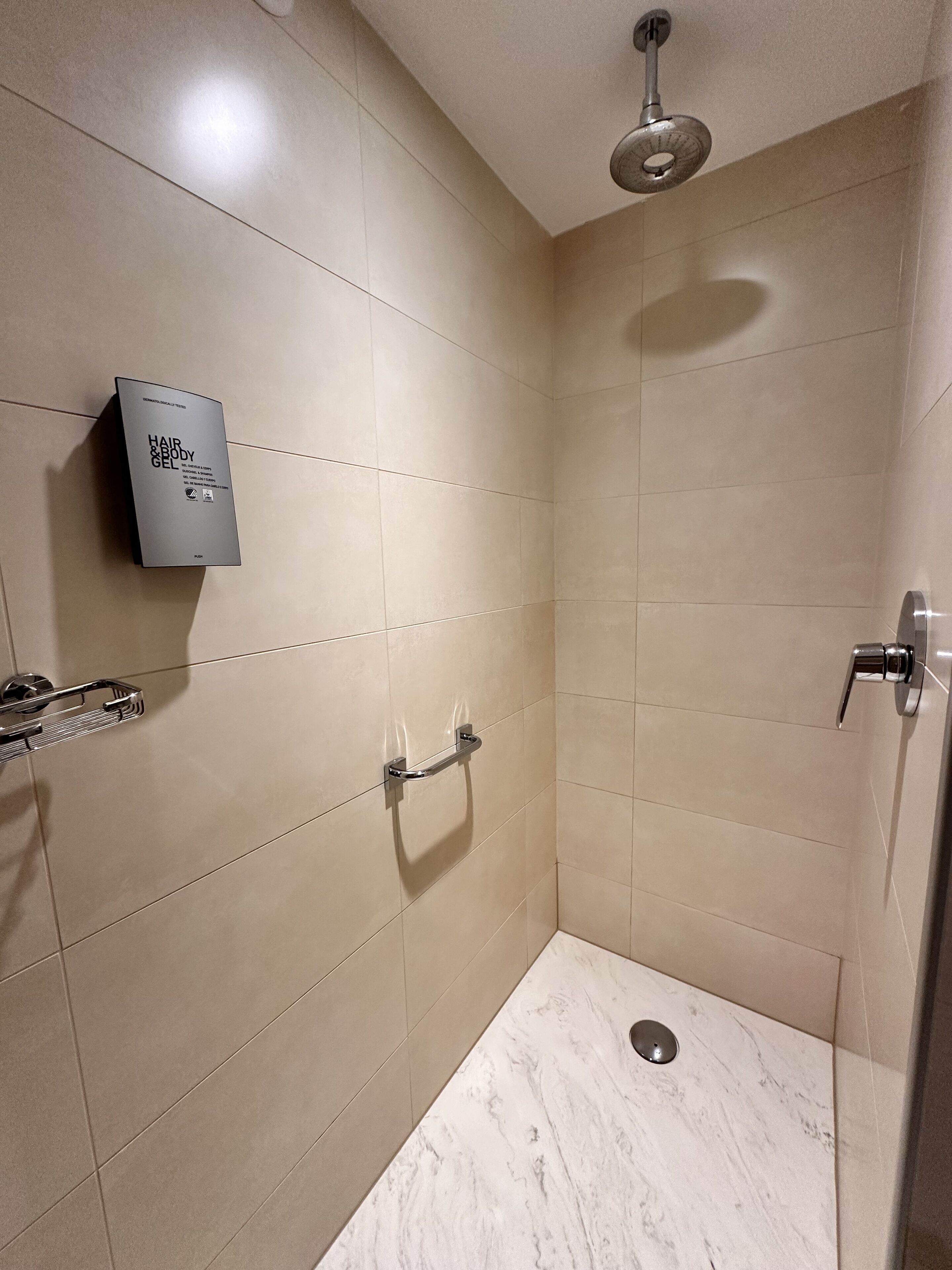 A modern bathroom with beige tiles, a handheld showerhead, a handheld showerhead, and a towel rack.