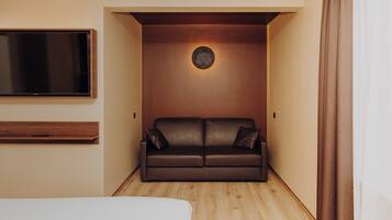 A modern hotel room with a brown leather sofa, a flat-screen TV mounted on the wall, and a wooden floor.
