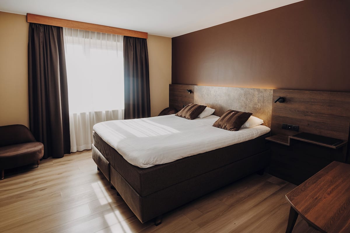 A modern hotel room with a large bed, a wooden nightstand, a desk, and a chair.