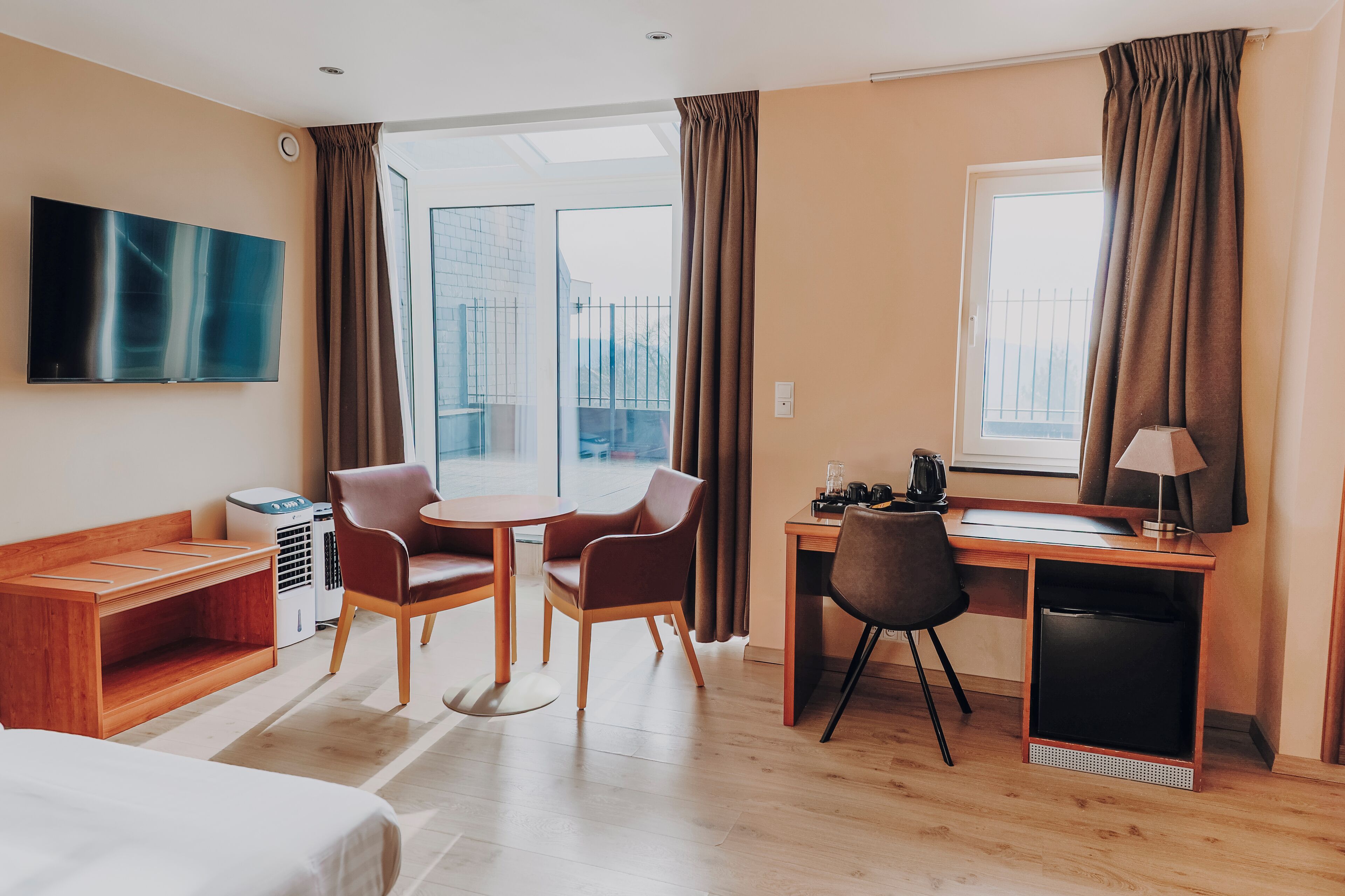 A hotel room with a bed, a desk with a chair, a TV, a window with curtains, and a view of the outside.