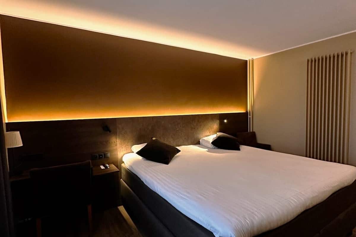 A hotel room with a large bed, a nightstand, a lamp, and a wall-mounted light fixture.
