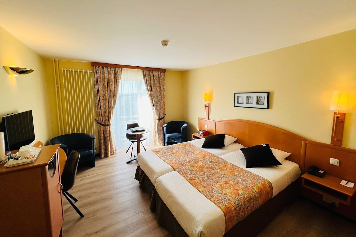 A hotel room with a bed, desk, chair, and a small table.
