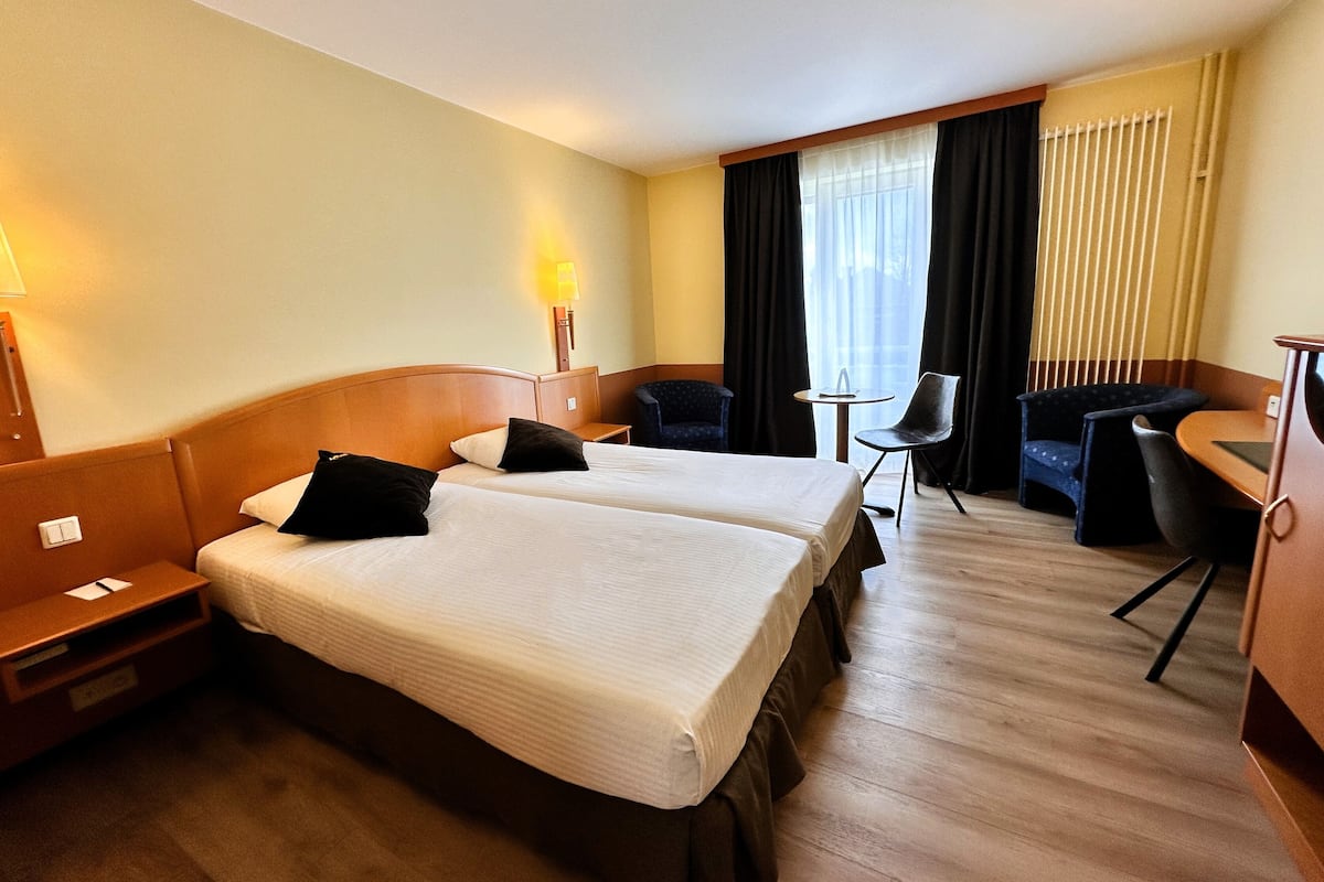 A hotel room with two beds, a desk, a chair, and a small table.